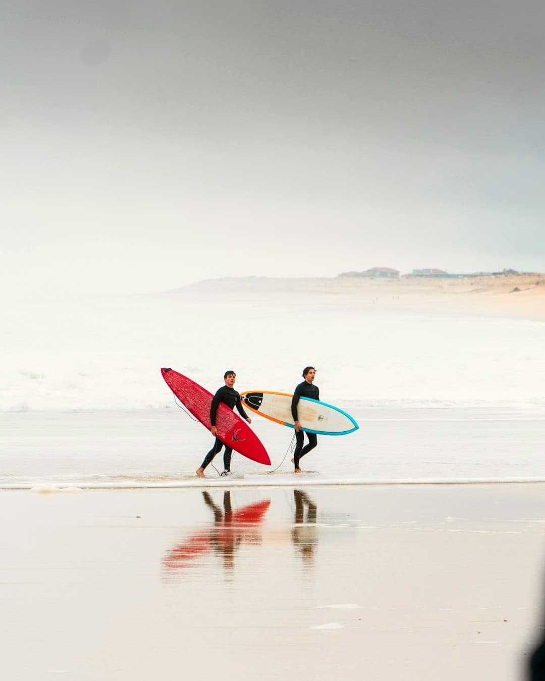 Two surfers carrying their boards along the shoreline