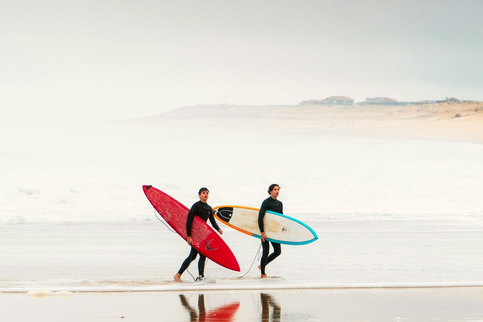 Two surfers carrying their boards along the shoreline